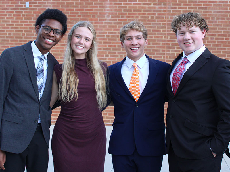 Four students in business attire pose for a group photo in front of the Student Union.